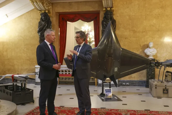 Two men in suits talk in the marble hall of Lancaster House in London beside a display of drones and a large uncrewed aircraft