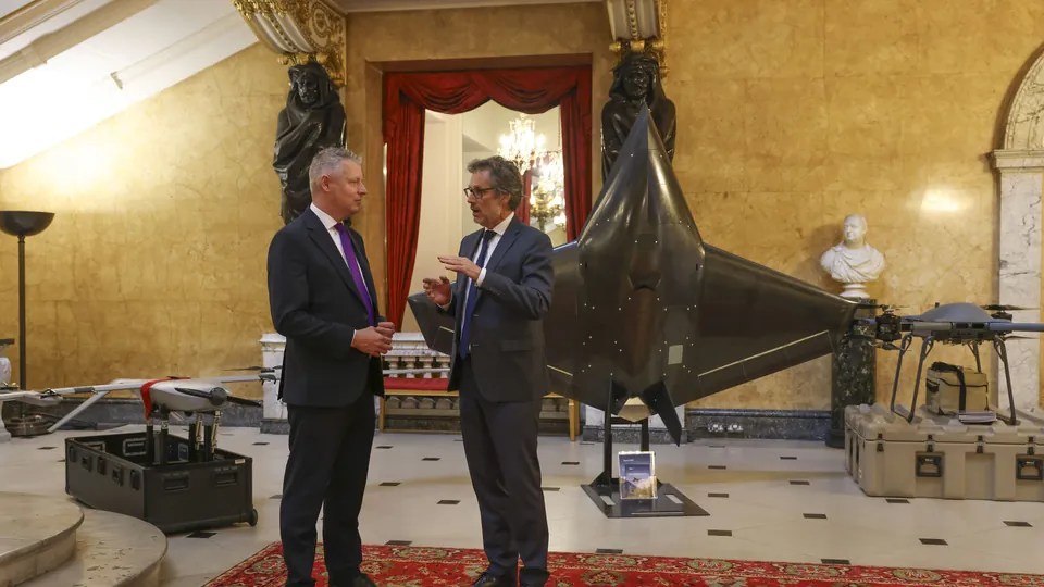 Two men in suits talk in the marble hall of Lancaster House in London beside a display of drones and a large uncrewed aircraft