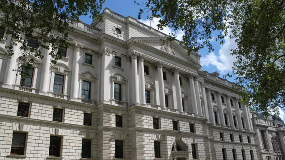 The stone facade of the HM Treasury building in Westminster, London, seen through trees