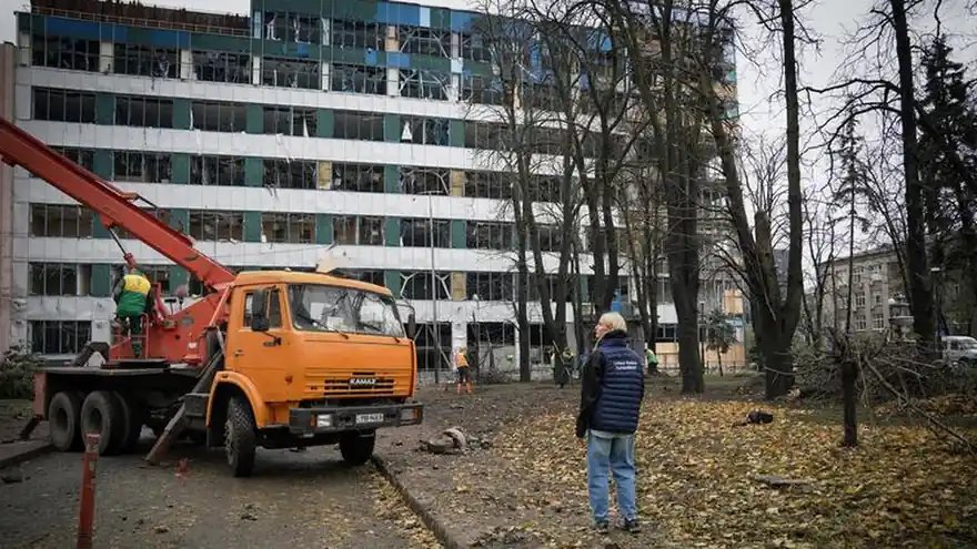 A crane truck and a UN humanitarian worker in front of a multi-storey building with blown-out windows in Ukraine