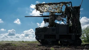 A camouflaged unmanned ground vehicle with a heavy machine gun in an open field