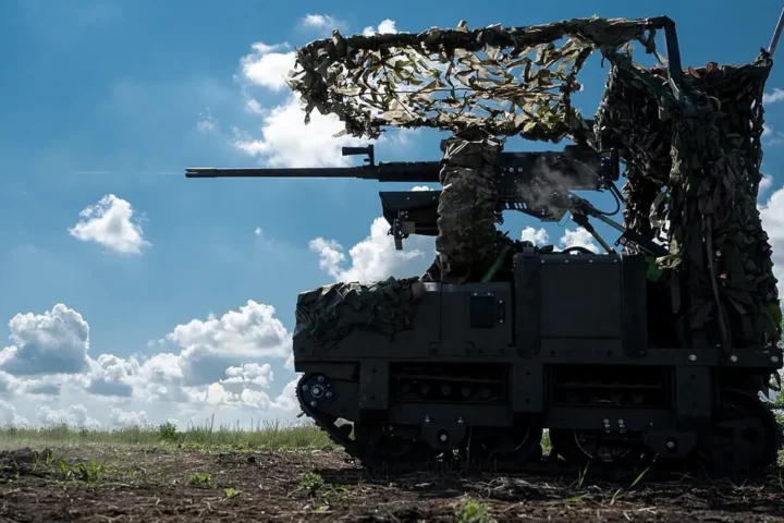 A camouflaged unmanned ground vehicle with a heavy machine gun in an open field