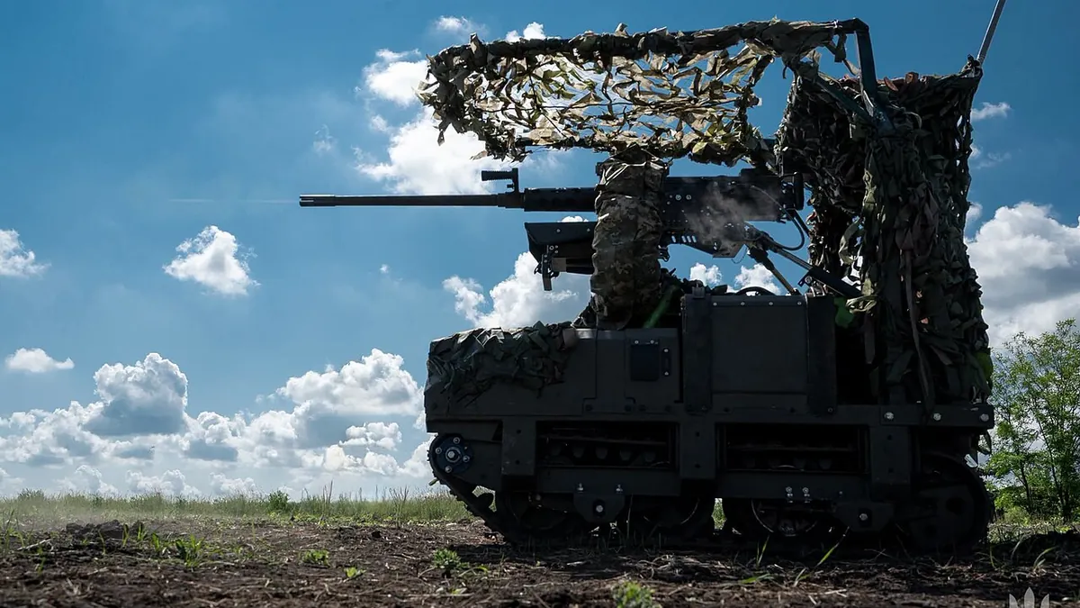 A camouflaged unmanned ground vehicle with a heavy machine gun in an open field