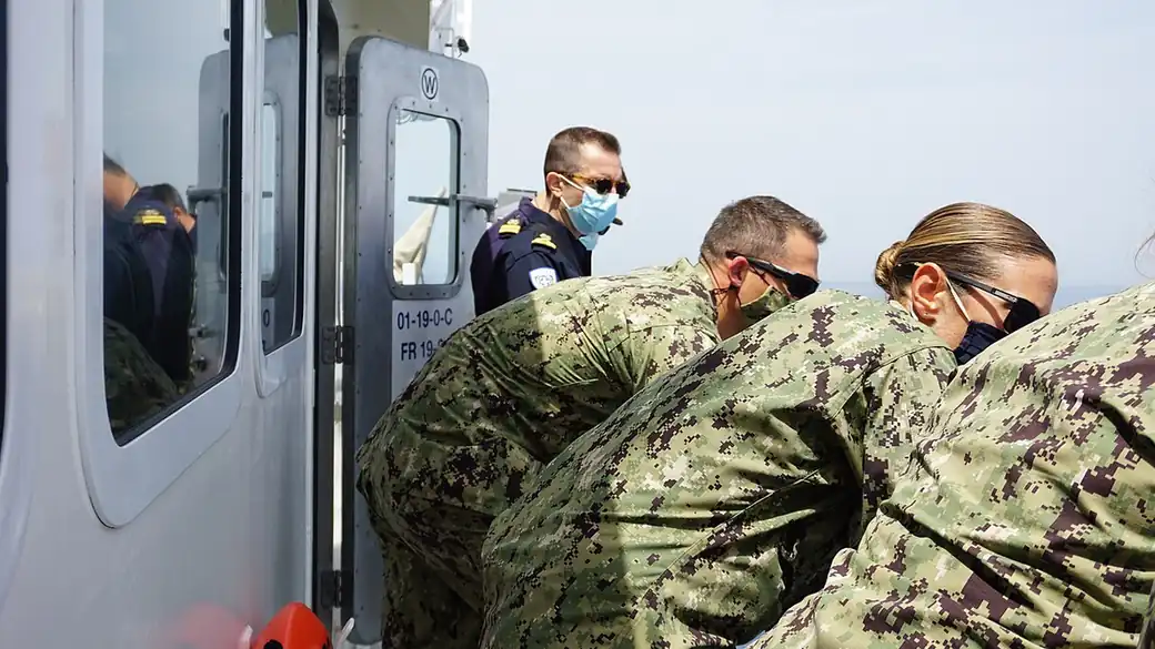 Hellenic Coast Guard officer and U.S. Coast Guard personnel on the deck of a vessel at sea during a joint rescue and assistance training exercise