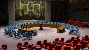 The empty Security Council chamber at UN headquarters in New York, with blue delegate chairs, red observer seats and a large mural