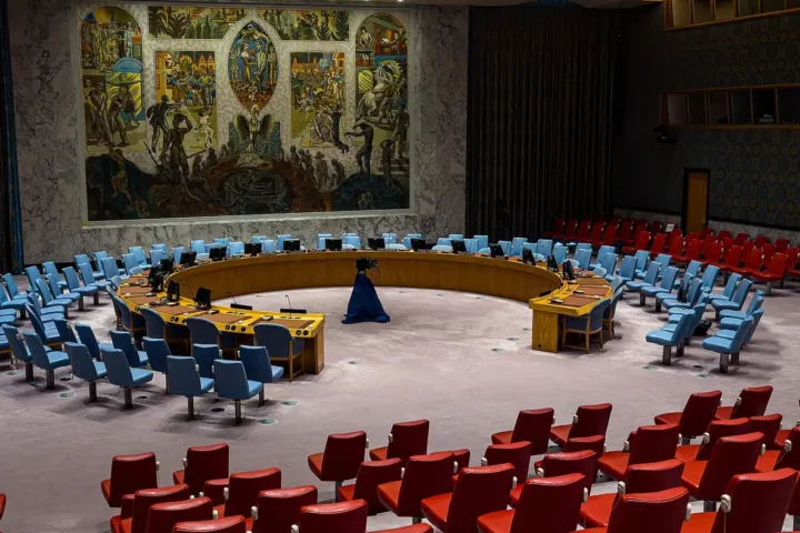 The empty Security Council chamber at UN headquarters in New York, with blue delegate chairs, red observer seats and a large mural