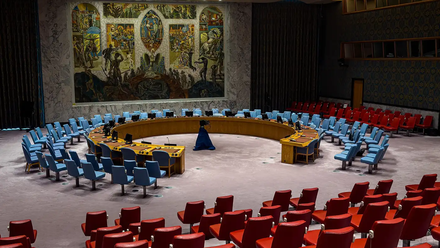 The empty Security Council chamber at UN headquarters in New York, with blue delegate chairs, red observer seats and a large mural