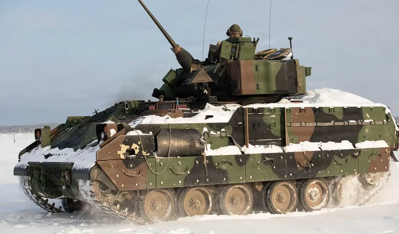 A US Army M2 Bradley fighting vehicle covered in snow driving across a snowy training area in Lithuania