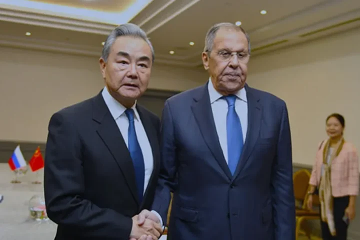 Chinese Foreign Minister Wang Yi and Russian Foreign Minister Sergei Lavrov shake hands in front of their national flags