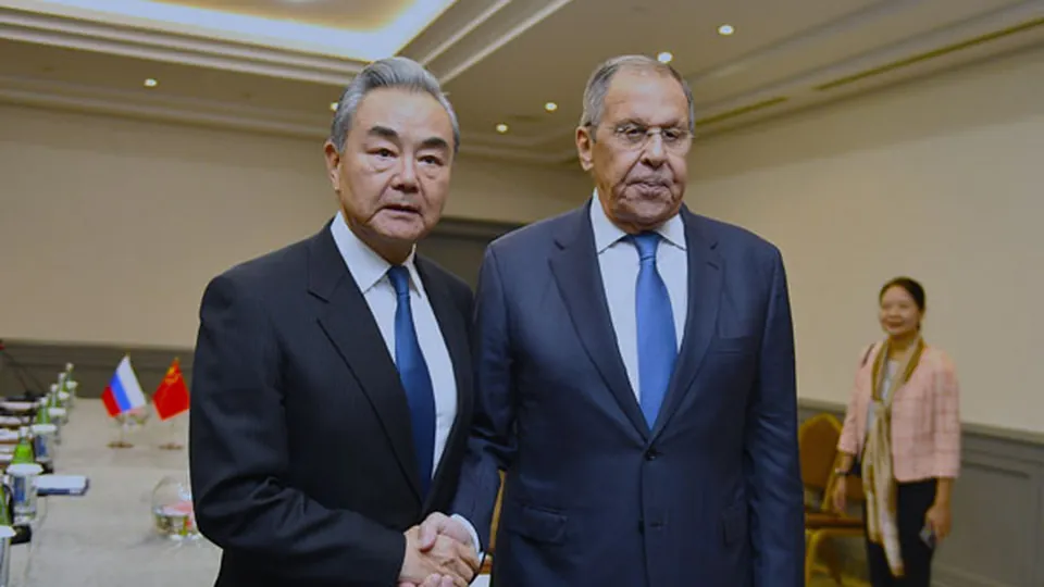 Chinese Foreign Minister Wang Yi and Russian Foreign Minister Sergei Lavrov shake hands in front of their national flags