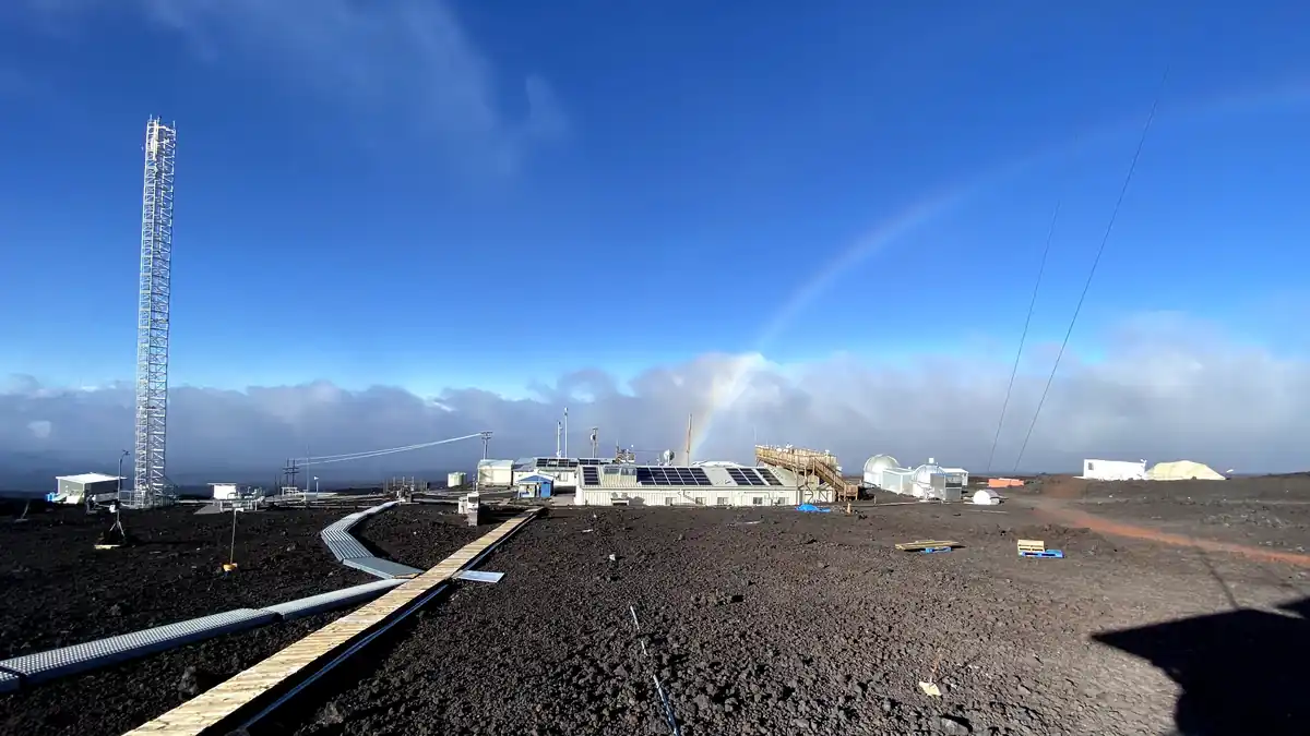 NOAA's Mauna Loa Observatory on Hawaii's volcanic terrain with a rainbow over the station buildings and a monitoring tower