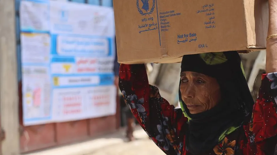 A woman carries a box of WFP food rations on her head in Jabal Habashi, Taiz governorate, Yemen