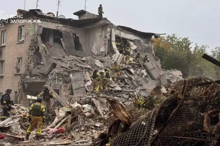 Rescuers in uniform search the rubble of a partly collapsed brick apartment building in Zaporizhzhia, with the State Emergency Service logo in the corner
